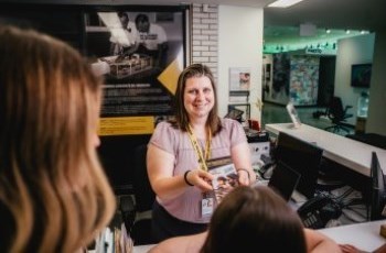 A woman standing behind the reception desk at the Oil Museum of Canada, handing a brochure to guests