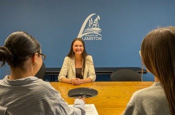 a person being interviewed by two interviewers against a blue wall with the County of Lambton logo